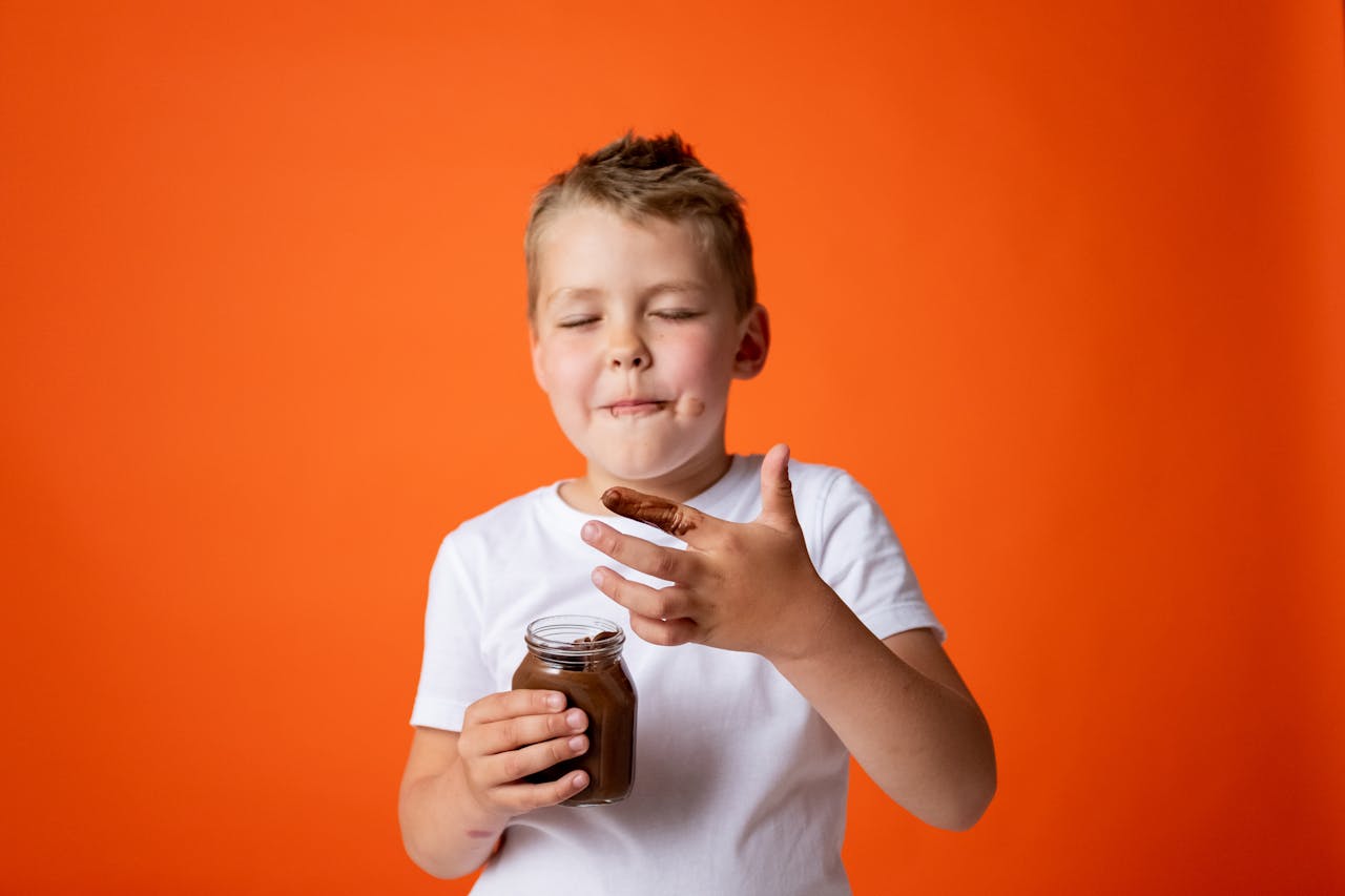 Adorable child savoring chocolate spread in a playful studio setting.